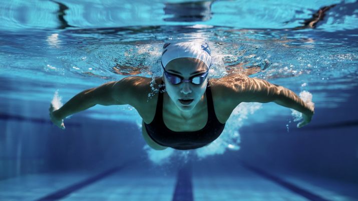 athletic woman swims underwater in a pool, wearing a black swimsuit, swim cap, and goggles. the light reflections on the water enhance the sense of motion and intensity of the sport.